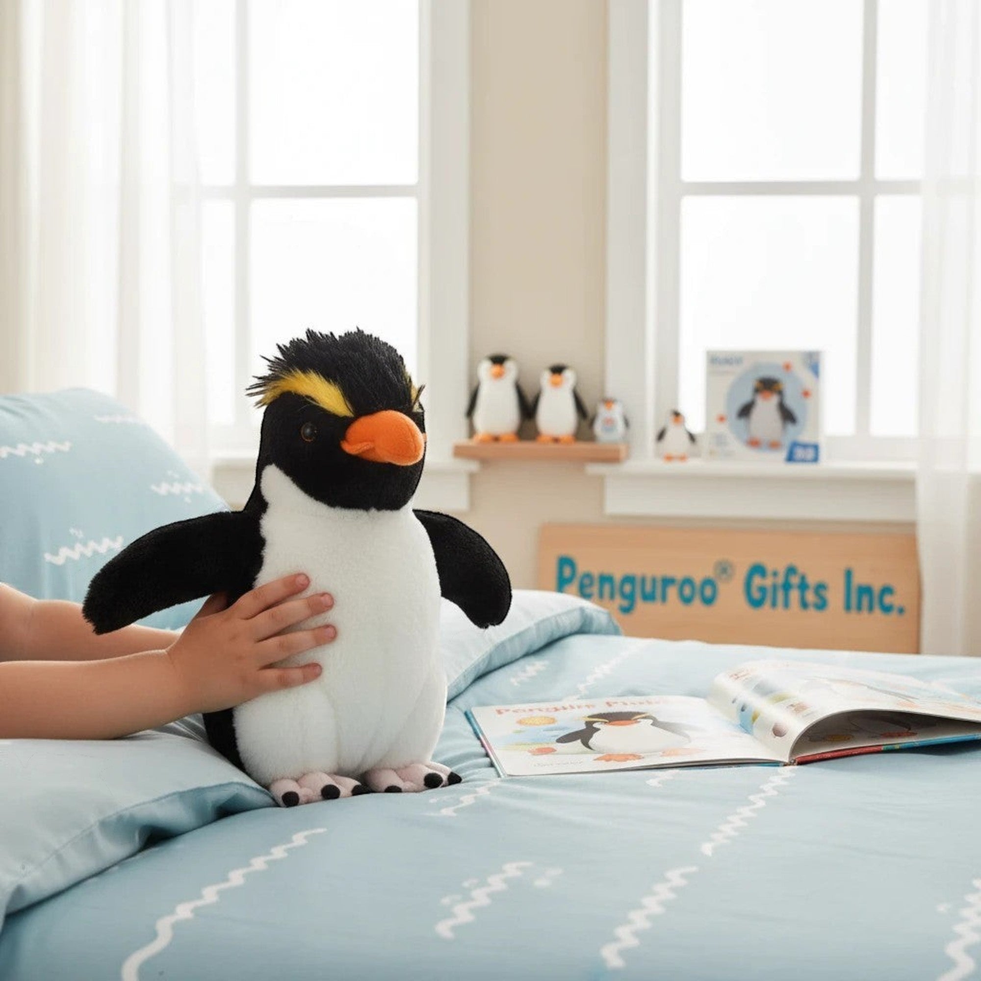 Penguroo Gifts Inc. plush penguin toy with black and white body, orange beak, and yellow crest, held by child on a bed.